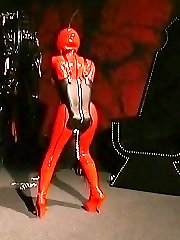 Busty slave in full red latex outfit, air hood and corset suffers in a punishment room