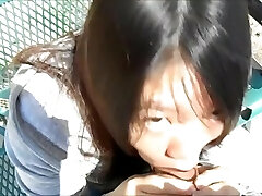 Asian woman blowing boys in the park in broad day light