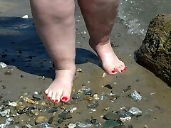 Phat bare legs with red pedicure walk along the bank of the river, fetish.