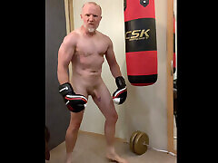 Aggressive muscular boxer working out naked with a punch bag and cums on his boxing gloves