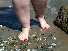 Good-sized bare legs with red pedicure walk along the bank of the river, fetish.