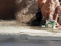 indische schwägerin badet im offenen hof des hauses, steckt einen finger in ihren bau und reibt den körper, schwägerin wäscht das badezimmer