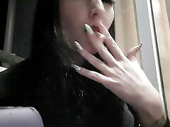 Dominatrix Nika smokes a cigarette on the balcony. Mistress sexy red lips blow smoke in your face